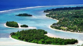 Aerial side-view image of a clear and calm Muri lagoon capturing the forest-covered islets on white sandy beaches with contrasting shades of blue waters of Rarotonga