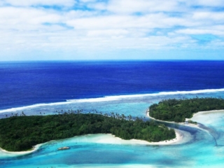 A breath-taking aerial view the forest-covered islets in Muri on a glowing white sandy beach with contrasting all-shades-of-blue waters of Rarotonga, also capturing a sailing boat berthed offshore