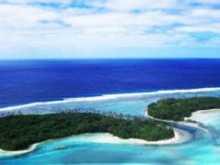 A breath-taking aerial view the forest-covered islets in Muri on a glowing white sandy beach with contrasting all-shades-of-blue waters of Rarotonga, also capturing a sailing boat berthed offshore