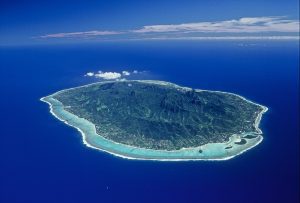 Aerial view of Rarotonga Island featuring a clear lagoon surrounded by coral reefs that separates the island from the appealing exquisite shade of rich royal blue of the ocean, evoking its depth