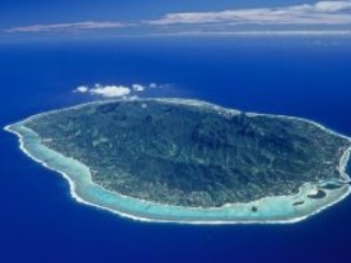 Aerial view of Rarotonga Island featuring a clear lagoon surrounded by coral reefs that separates the island from the appealing exquisite shade of rich royal blue of the ocean, evoking its depth
