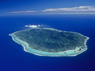 Aerial view of Rarotonga Island featuring a clear lagoon surrounded by coral reefs that separates the island from the appealing exquisite shade of rich royal blue of the ocean, evoking its depth