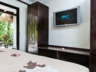 image of a flat TV screen mounted on to a wall between two tall carved-Polynesian-style deep brown colour wardrobes, a view from the super king bed
