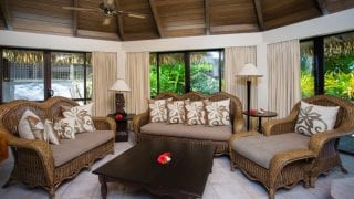 A luminous living room of the Premium Beachfront Villa showcasing the polished brown furniture with contrasting background featuring a tropical lush garden