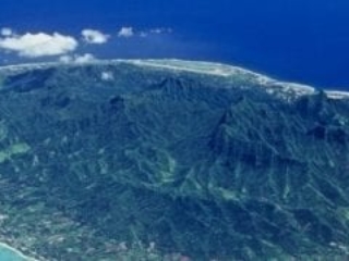 Aerial view of Rarotonga Island featuring a clear lagoon surrounded by coral reefs that separates the island from the appealing exquisite shade of rich royal blue of the ocean, evoking its depth