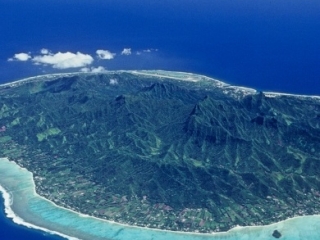 Aerial view of Rarotonga Island featuring a clear lagoon surrounded by coral reefs that separates the island from the appealing exquisite shade of rich royal blue of the ocean, evoking its depth
