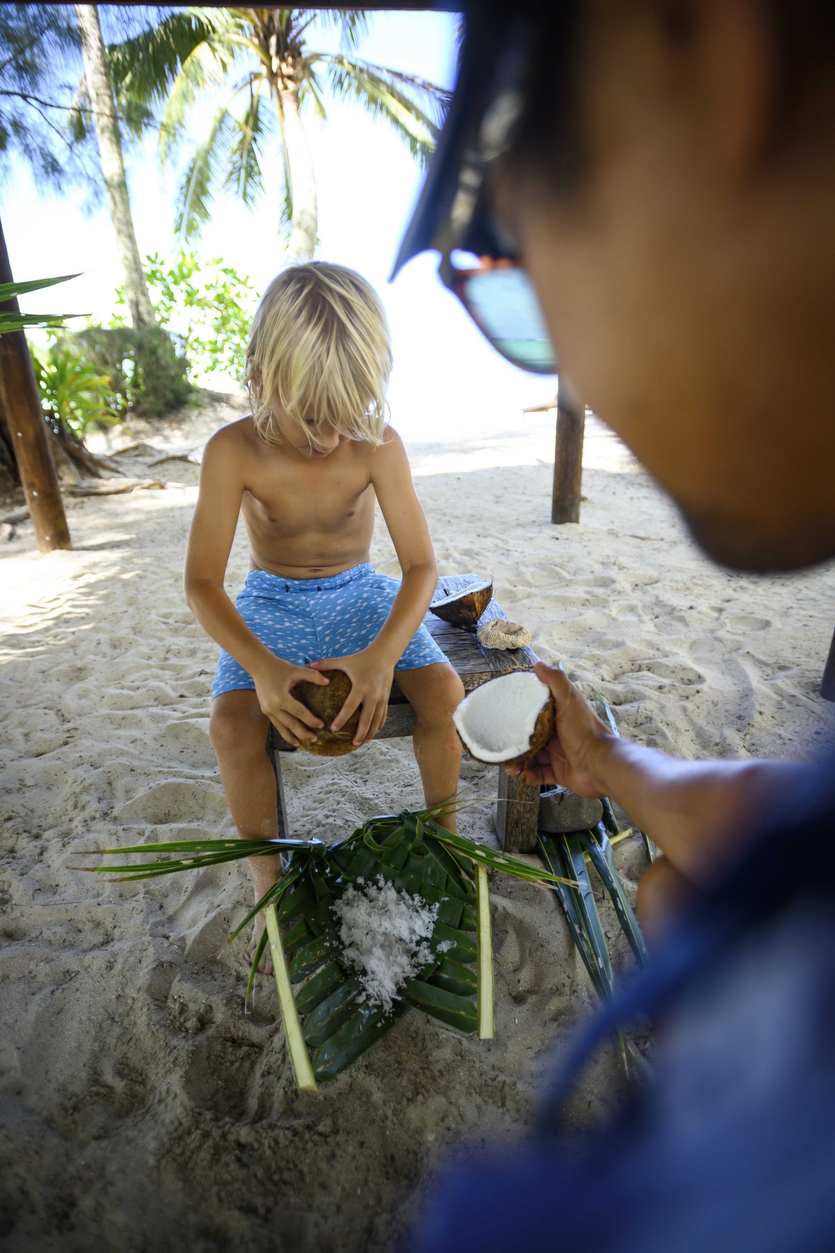 a kid demonstrating his coconut scraping skills by the beach as part of the Beach Hut kids' activity
