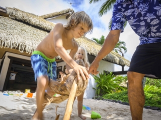 a kid learns to husk a coconut with the help of a Beach Hut attendant