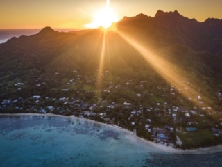 A stunning aerial image of the South-Eastern side of Rarotonga Island capturing a glorious and breathtaking sunset in the background which illuminates the horizon