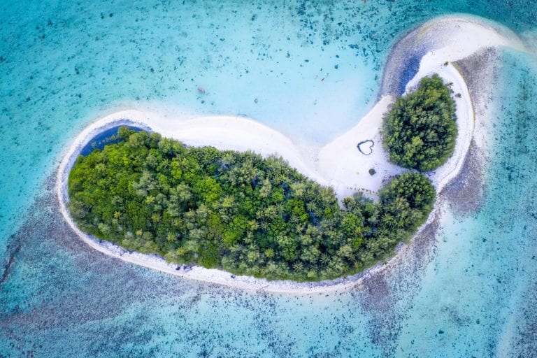 a stunning aerial image of the islets in the Muri lagoon capturing a heart symbol printed on a glowing white sandy beach