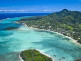 A stunning aerial image of Rarotonga Island featuring green peaks and a aqua-coloured lagoon set amidst a clear deep blue coloured Ocean