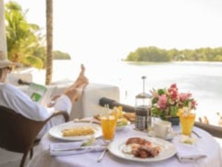 Guest enjoys room-serviced-breakfast in the comfort of her private Premium Beachfront Suite balcony, overlooking the Muri Lagoon