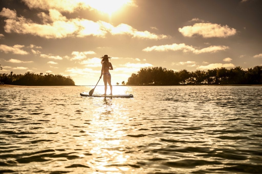 image of a lady standing on a Stand-Up-Paddle board holding a paddle while looking at the amazing sunset that illuminates the atmosphere