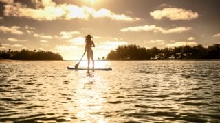 image of a lady standing on a Stand-Up-Paddle board holding a paddle while looking at the amazing sunset that illuminates the atmosphere