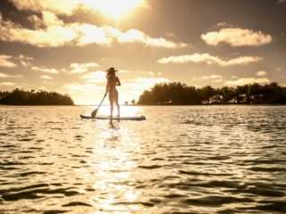 image of a lady standing on a Stand-Up-Paddle board holding a paddle while looking at the amazing sunset that illuminates the atmosphere